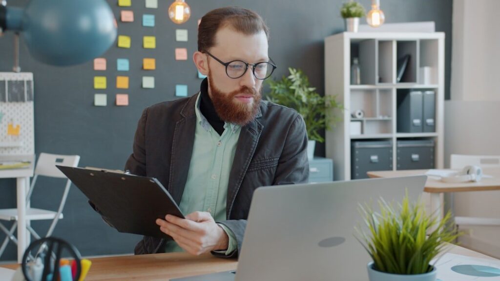 businessman taking notes looking at laptop screen working in creative office at desk. Modern people, workplace and information concept.