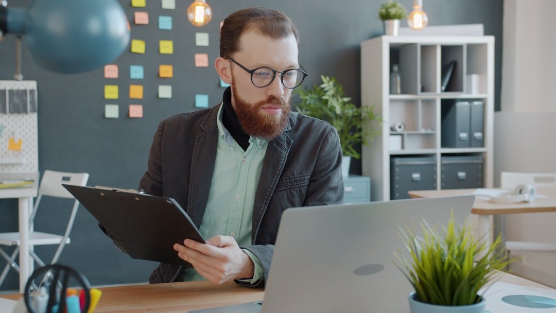 businessman taking notes looking at laptop screen working in creative office at desk. Modern people, workplace and information concept.